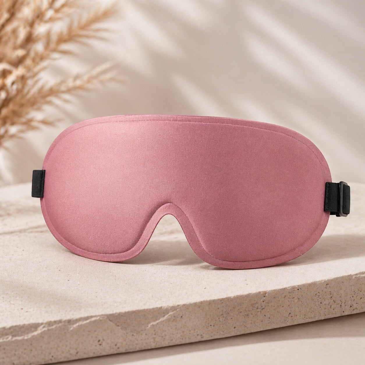 SlumberHush DeepShield pink satin sleep mask with adjustable black straps, contoured for comfort.