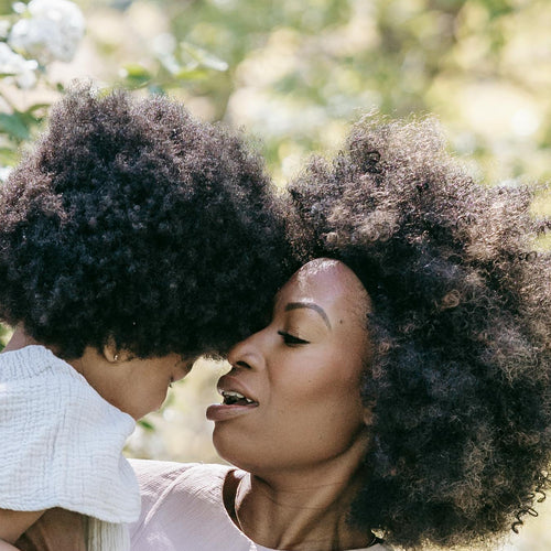 Woman holding a child in a park with white flowers and trees in the background