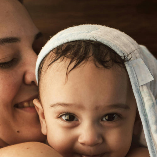 Woman holding a baby wrapped in a towel, both smiling.