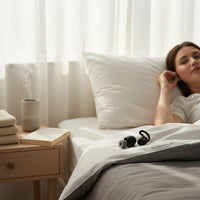 SlumberHush QuietSeal earplugs in black with grey tips, designed for sleep, shown on a bed next to a woman.